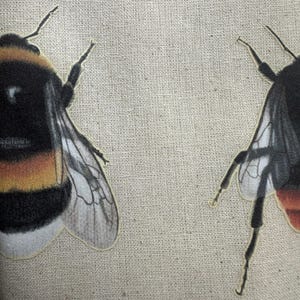 Op de afbeelding: Twee hommels met zwarte en gele strepen en doorschijnende vleugels zijn genaaid op een beige canvas stof.