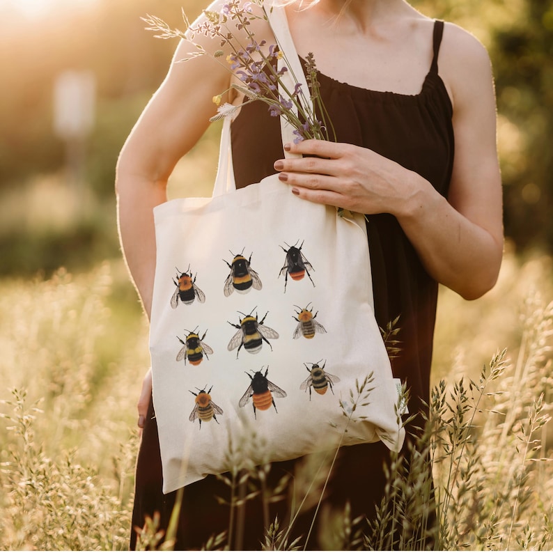 Op de afbeelding: Een witte tote bag met een ontwerp van negen hommels in verschillende poses. De bijen zijn ge&iuml;llustreerd in tinten zwart, geel en oranje.