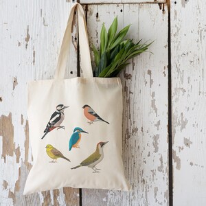 Puede incluir: Una bolsa de lona blanca con cinco ilustraciones de p&aacute;jaros coloridos. Los p&aacute;jaros son un p&aacute;jaro carpintero, un petirrojo, un mart&iacute;n pescador, un p&aacute;jaro carpintero verde y un jilguero.