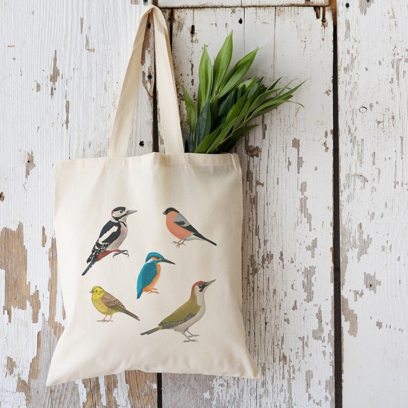 Puede incluir: Una bolsa de lona blanca con cinco ilustraciones de p&aacute;jaros coloridos. Los p&aacute;jaros son un p&aacute;jaro carpintero, un petirrojo, un mart&iacute;n pescador, un p&aacute;jaro carpintero verde y un jilguero.