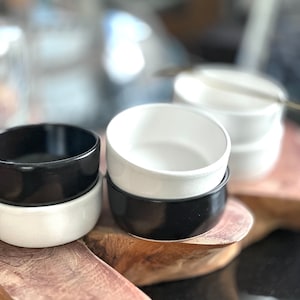 May include: Two sets of stacked bowls, one set is black and white, the other is white and black. The bowls are sitting on a wooden surface.