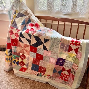 May include: A handmade patchwork quilt featuring a variety of square fabric blocks in red, blue, yellow, pink, and white with diverse floral, plaid, and geometric patterns. The quilt is tied with small white yarn knots throughout the surface.