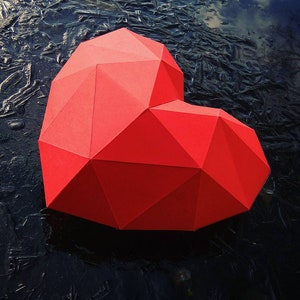 May include: A red origami heart with a geometric design, lying on a black surface.