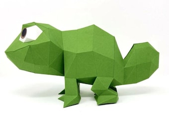 May include: A green papercraft chameleon with a large eye, standing on a white surface.