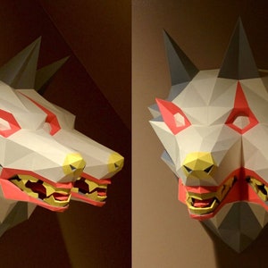 May include: A two-headed wolf sculpture made of paper. The sculpture is painted in shades of grey, white, red, and yellow. The wolf's eyes are red, and its teeth are yellow.