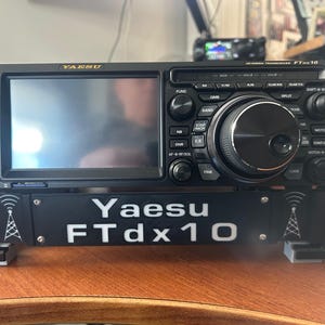 May include: A black Yaesu FTdx10 HF/50MHz transceiver with a large display screen and numerous control knobs and buttons. The unit has the Yaesu logo and model number printed on the front panel. The transceiver is designed for amateur radio use.