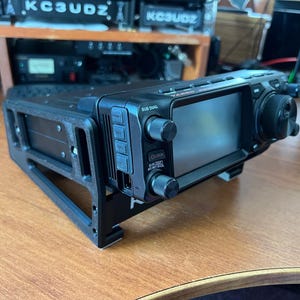 May include: A white ceramic mug with a black handle and the text "But First, Coffee" in a bold, black font. The mug is filled with a dark liquid, probably coffee, and rests on a light-coloured surface.