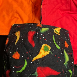 May include: Four fabric pot holders, one with a black background and red, yellow, and green chili pepper print, one orange, one red, and one yellow.