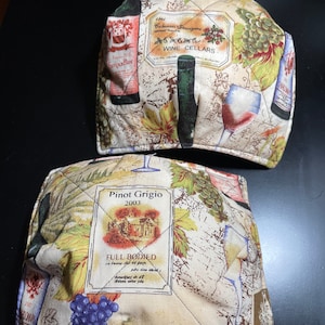 Könnte beinhalten: Zwei gequiltete Topflappen mit Wein-Motiv. Der obere Topflappen zeigt ein Weinetikett mit dem Text "Cabernet Sauvignon Wine Cellars 1981". Der untere Topflappen zeigt ein Weinetikett mit dem Text "Pinot Grigio 2003 Full Bodied".