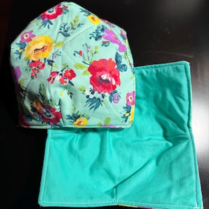 May include: A set of two teal blue quilted pot holders with a floral print. The top pot holder is folded in half and the bottom pot holder is flat.