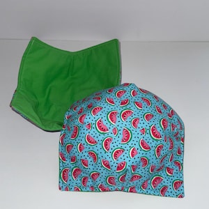 Puede incluir: Dos fundas de tela para cuencos. Una se muestra con el interior hacia arriba, revelando una tela verde brillante lisa. La otra está colocada delante, mostrando un patrón exterior de pequeñas rodajas de sandía rosas sobre azul claro.