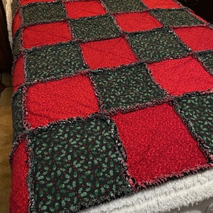 May include: A red and green patchwork quilt with a holly leaf pattern. The quilt is made of squares and has a ruffled edge.