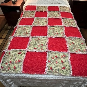 Peut inclure: Une courtepointe patchwork avec des carrés rouges et à motifs. Les carrés à motifs présentent des cardinaux rouges sur un fond vert. La courtepointe est sur un lit avec un couvre-lit blanc texturé.