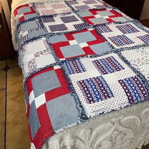 May include: A red, white and blue patchwork quilt with a frayed edge. The quilt is made of various fabrics, including denim, stars and polka dots.