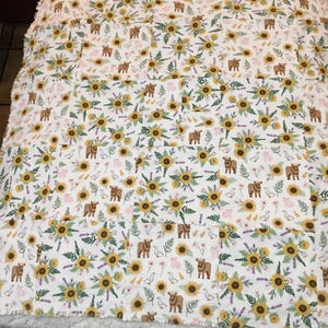 May include: White quilt with a repeating pattern of yellow sunflowers, brown cows, and lavender sprigs. The quilt has a soft, textured border. The design combines floral and farm animal elements.
