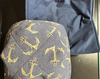May include: Two navy blue bowl cozies. One is a solid navy blue, and the other is a navy blue fabric with a repeating pattern of yellow anchors. The anchor cozy is quilted.