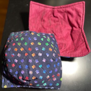 Puede incluir: Un juego de dos protectores de cuenco acolchados. Uno es azul oscuro con un patrón de huellas de patas arcoíris y el otro es burdeos sólido.