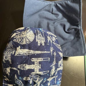 Könnte beinhalten: Zwei marineblaue Stoff-Schüsseluntersetzer. Einer hat ein weißes und blaues Weltraum-Muster mit verschiedenen Raumschiffen. Der andere ist einfarbig marineblau. Diese Untersetzer schützen die Hände vor heißen Schüsseln.