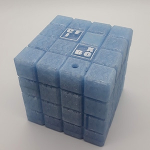 May include: A light blue cube-shaped object with the text "ICE BOX" printed on the top. The cube is made of smaller, textured blocks. A small hole is visible on the top. The object is likely a container or a decorative item.