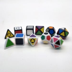 Puede incluir: Una colección de coloridos juguetes de rompecabezas geométricos en varias formas, incluyendo cubos, triángulos y figuras de múltiples lados. Los juguetes presentan una mezcla de colores primarios y secundarios, con acentos en blanco y negro. Las formas tienen un diseño de balón de fútbol.