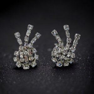 May include: A pair of silver earrings with a cluster of clear rhinestones in a geometric design.
