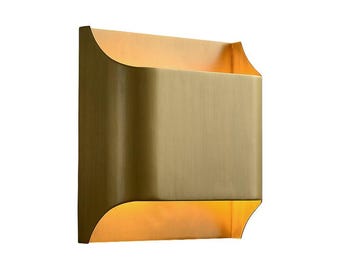 May include: A brass wall sconce with a curved, rectangular shape. The light fixture has a warm, golden glow.