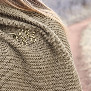 Puede incluir: Primer plano de un suéter de punto marrón con un accesorio para el cabello de alambre dorado en forma de nudo.