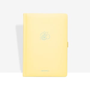 Könnte beinhalten: Ein hellgelbes Notizbuch mit einer hellblauen Zitronenillustration und dem Wort "JOURNAL" unten. Das Notizbuch hat einen glatten Einband und einen Laschenverschluss auf der rechten Seite.