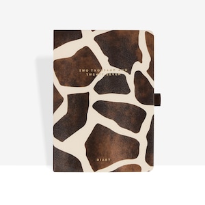 Puede incluir: Una agenda rectangular con un patrón de jirafa en color marrón y crema en la cubierta. El texto "TWO THOUSAND AND TWENTY SEVEN" está impreso en dorado cerca de la parte superior, y la palabra "DIARY" está impresa en dorado en la parte inferior central.