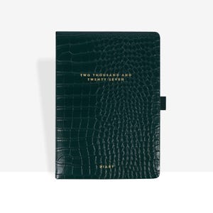 Op de afbeelding: Een donkergroene agenda met een textuur van krokodillenleer. De kaft is voorzien van goudkleurige tekst met TWO THOUSAND AND TWENTY SEVEN bovenaan en DIARY onderaan. Aan de rechterkant van de kaft bevindt zich een zwarte elastische penlus.