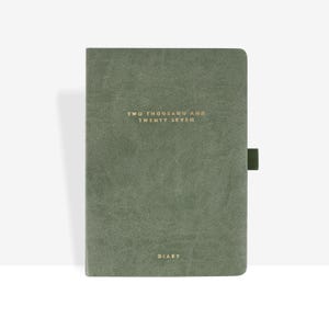 May include: A sage green diary with a textured cover featuring the gold embossed text TWO THOUSAND AND TWENTY SEVEN and the word DIARY at the bottom. The notebook includes a matching green elastic pen loop attached to the right side edge.
