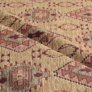 Puede incluir: Primer plano de una tela doblada con un patrón geométrico. La tela presenta un fondo beige con diseños repetidos en tonos burdeos, óxido y verde oliva. El patrón incluye formas de diamante y rectangulares.
