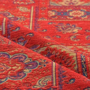 Puede incluir: Tela roja estampada con una superficie texturizada. La tela tiene un diseño repetitivo de motivos florales azules y dorados.