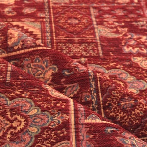 May include: Close-up of a richly textured, patterned fabric in shades of burgundy, tan, and blue. The design features repeating floral and geometric motifs, creating a vintage or traditional aesthetic. The fabric appears to be woven.
