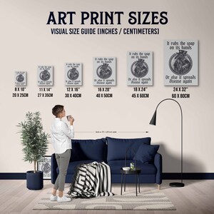 May include: A visual guide showing different art print sizes in inches and centimeters. The image shows a person standing in front of a couch and a floor lamp. The art prints feature a vintage illustration of a person wearing a mask and the text "It rubs the soap on its hands. Or else it spreads disease again."