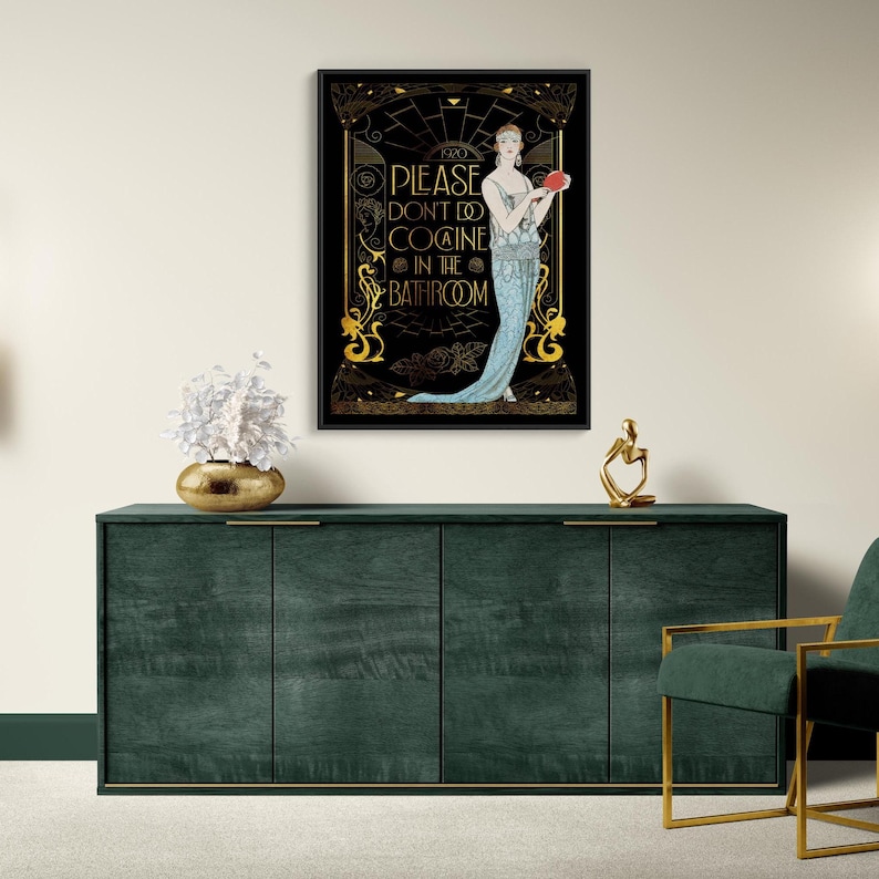 May include: A framed art print featuring a woman in a blue dress holding a red object, with the text "PLEASE DON'T DO COCAINE IN THE BATHROOM" in gold lettering. The artwork is displayed above a dark green cabinet.