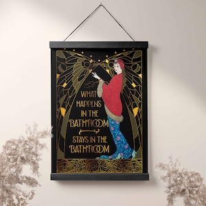 May include: A black and gold art print with a woman in a red and blue dress. The print has the text "What happens in the bathroom stays in the bathroom".