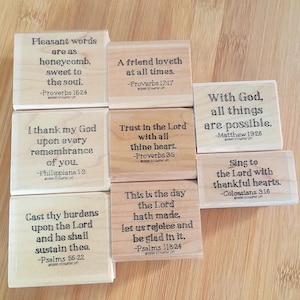 May include: A collection of wooden stamps with inspirational quotes from the Bible. The stamps feature phrases like "Pleasant words are as honeycomb" and "With God, all things are possible." The text is in a black, classic font.