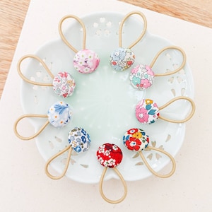 May include: A set of nine hair scrunchies featuring floral patterns. Each scrunchie has a unique floral design and colour combination. The scrunchies are made from soft fabric and are ideal for keeping hair in place.