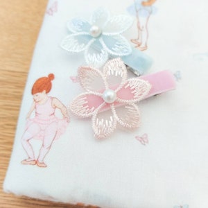 May include: Two hair clips with pink and blue velvet ribbon and a flower design. The flowers are made of sheer fabric with a pearl in the center.