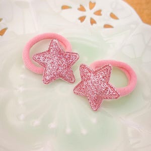 Pu&ograve; includere: Due elastici per capelli rosa con ciondoli a forma di stella rosa scintillante.