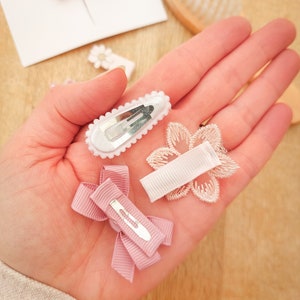 以下が含まれることがあります： ピンクと白のヘアクリップ4個セット。クリップはリボン、花、レースで飾られています。