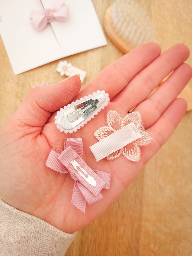 以下が含まれることがあります： ピンクと白のヘアクリップ4個セット。クリップはリボン、花、レースで飾られています。