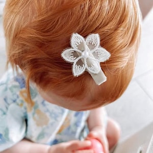 May include: A white flower hair clip with a pearl center. The clip is in a young person's red hair.