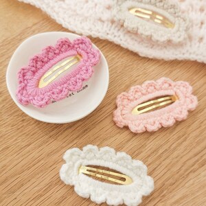 May include: Three crocheted hair clips in pink, light pink, and white. Each clip has a gold metal bar and a scalloped edge.