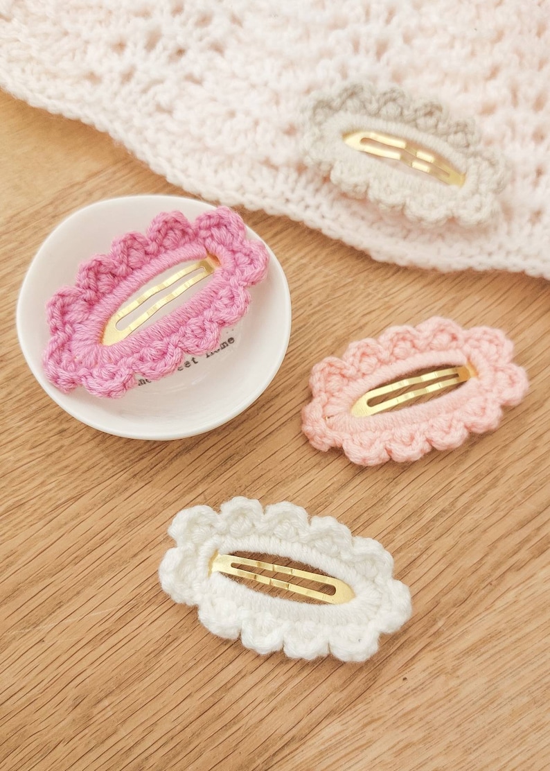 May include: Three crocheted hair clips in pink, light pink, and white. Each clip has a gold metal bar and a scalloped edge.