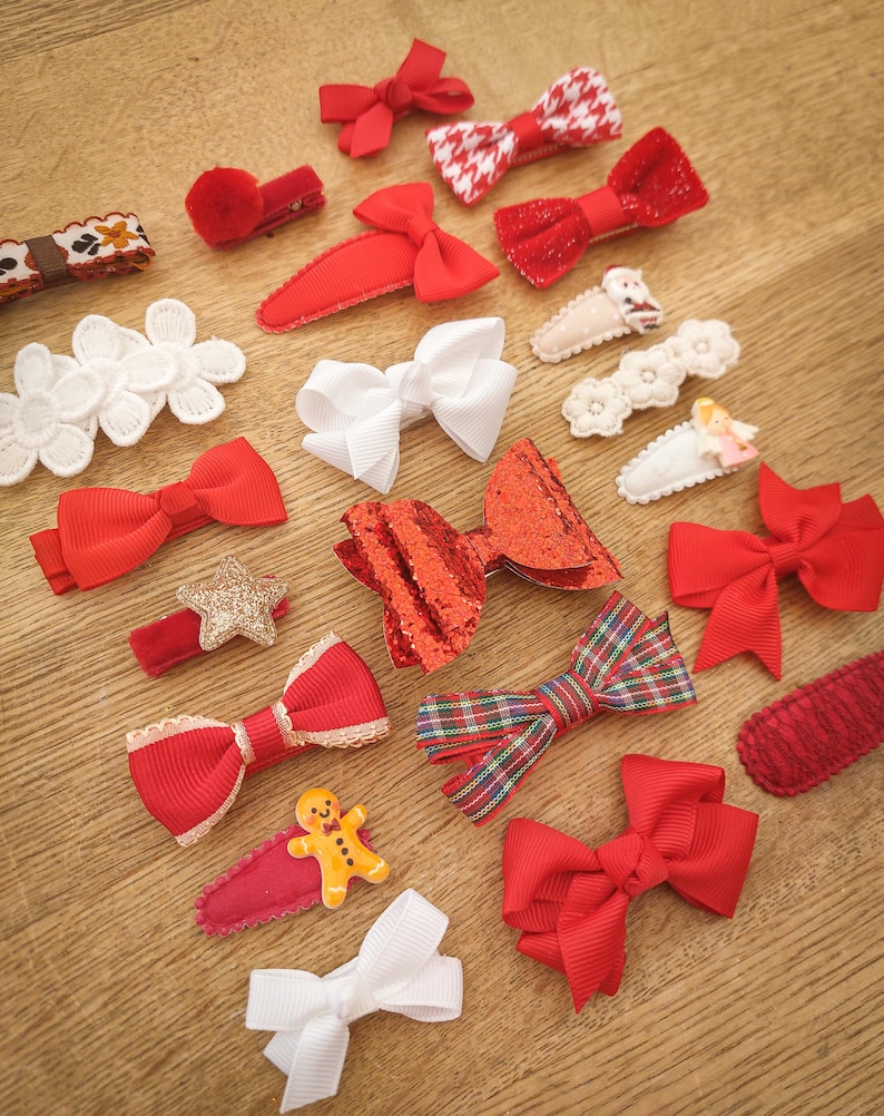 May include: A collection of red and white hair bows with various designs, including plaid, glitter, and polka dots. The bows are attached to alligator clips.