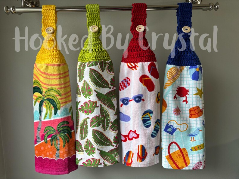 May include: Four hanging kitchen towels with crochet tops and button closures. The towels feature colorful beach-themed patterns, including palm trees, tropical leaves, and beach accessories. The crochet tops are yellow, green, red, and blue.