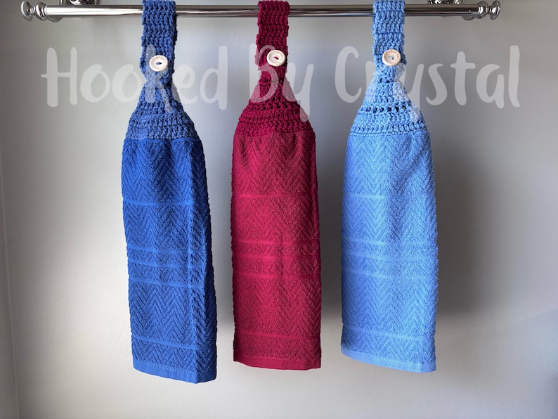 Pode incluir: Tr&ecirc;s toalhas de cozinha penduradas em azul royal, magenta escuro e azul claro, cada uma com um topo de croch&ecirc; com fecho de bot&atilde;o de madeira. As toalhas t&ecirc;m um padr&atilde;o de chevron texturizado e est&atilde;o suspensas numa barra de metal prateado.