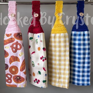 Pode incluir: Quatro panos de prato pendurados com topos de croch&ecirc; em rosa, vermelho, amarelo e azul, cada um preso com um bot&atilde;o de madeira. As toalhas apresentam padr&otilde;es de produtos de padaria, frutas e vegetais, xadrez amarelo e xadrez azul.
